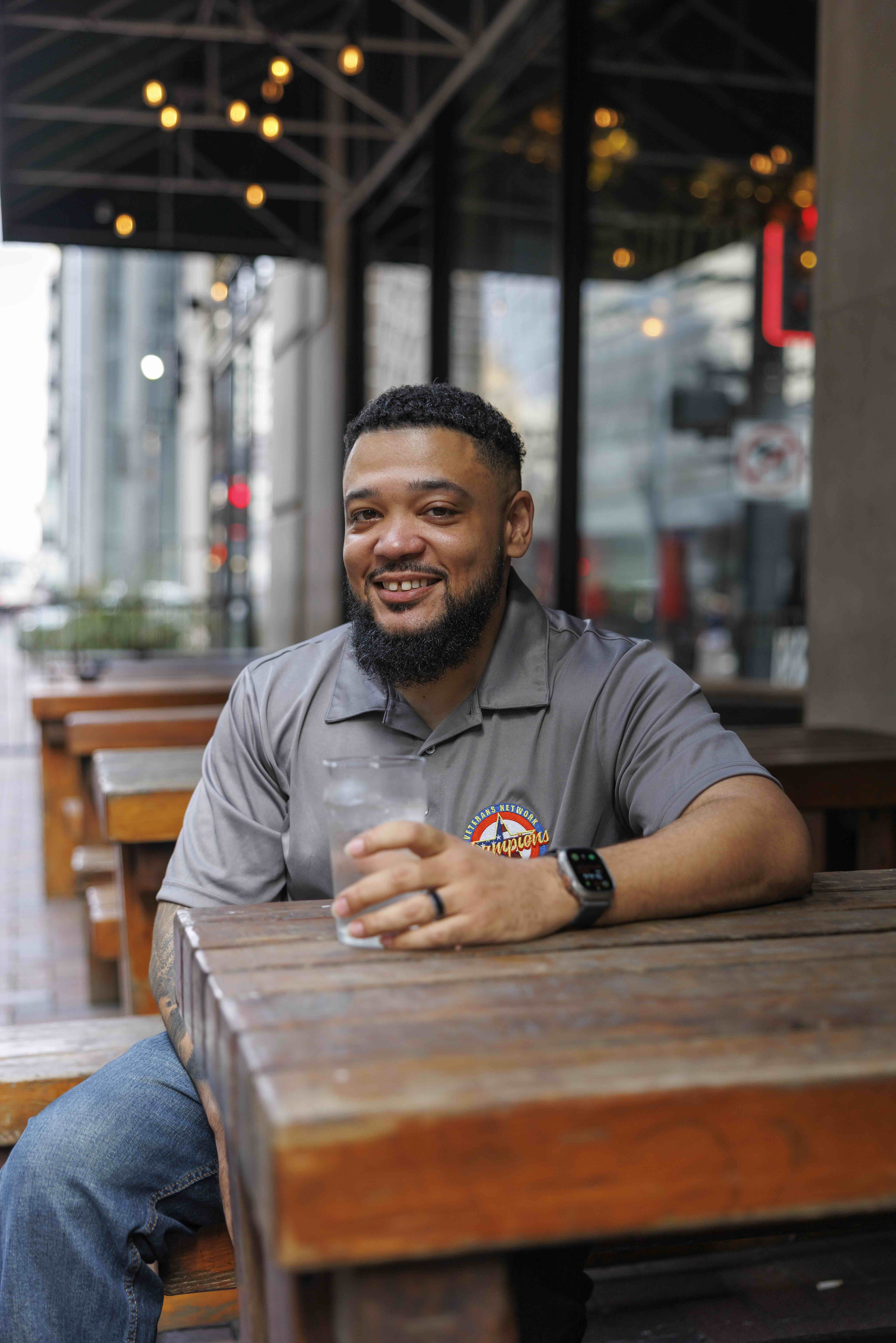 DP seated outside of restaurant looking at camera smiling holding a glass of water